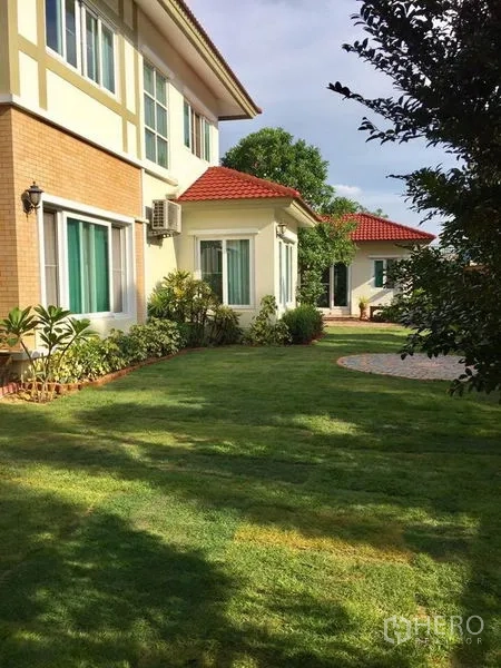 独立式住宅 出售在Pak Kret, Nonthaburi - 房屋侧面，红色瓦顶与宽阔的景观草坪。