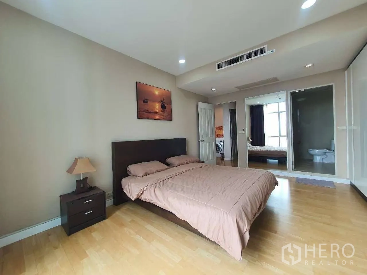 Condominium for rent in Khlong San, Bangkok - Spacious bedroom with king bed, wood floors, bedside table, and an en-suite bathroom visible through glass.