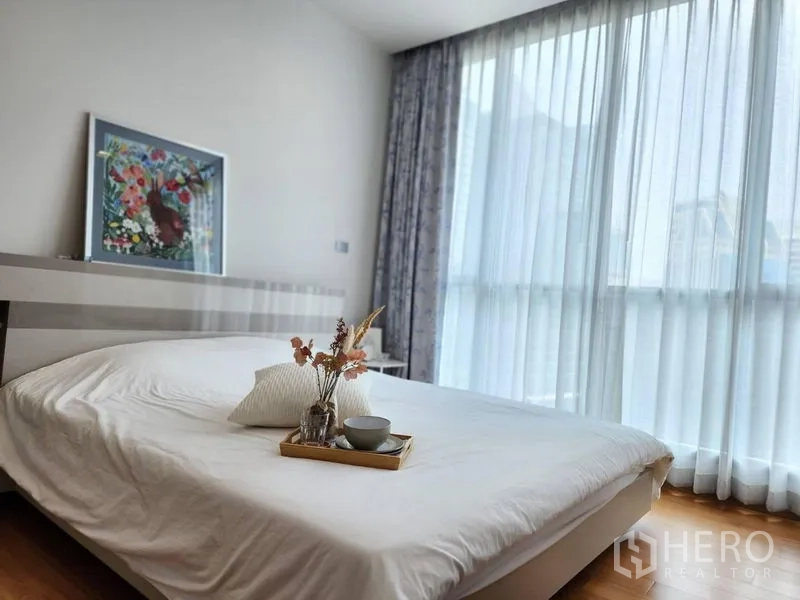 Condominium for rent in Watthana, Bangkok - Sunlit bedroom with large windows, sheer curtains and white bedding.