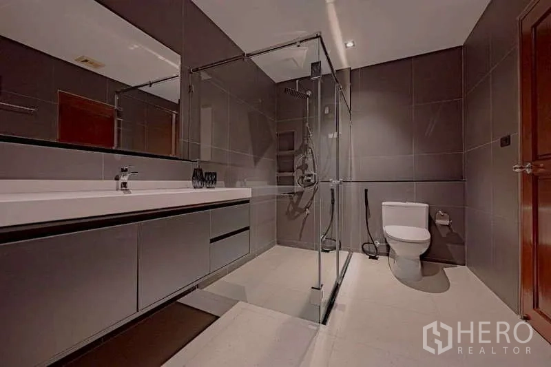 Detached House for rent or sale in Phra Khanong, Bangkok - Contemporary bathroom with a walk-in glass shower, long vanity, and WC.