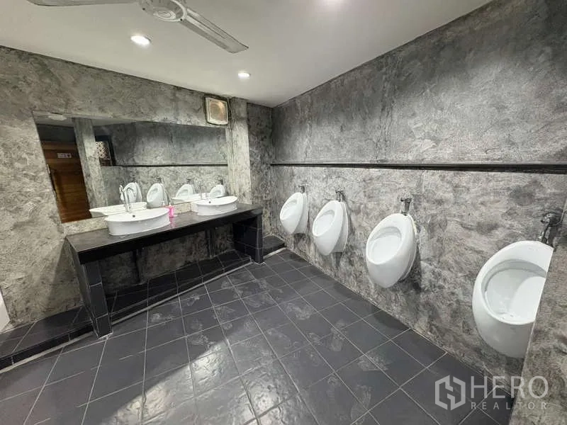 Standalone for rent in Khlong Toei, Bangkok - Men’s restroom with urinals and double vanity on dark tiles.