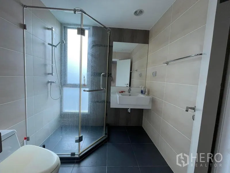 Condominium for sale in Sathon, Bangkok - Modern bathroom featuring a glass shower enclosure, beige wall tiles and a floating sink.