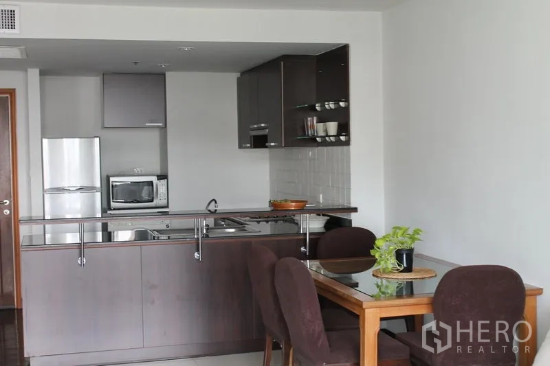 Apartment for rent in Bang Rak, Bangkok - Dining area beside a compact kitchen with stainless sink and appliances.