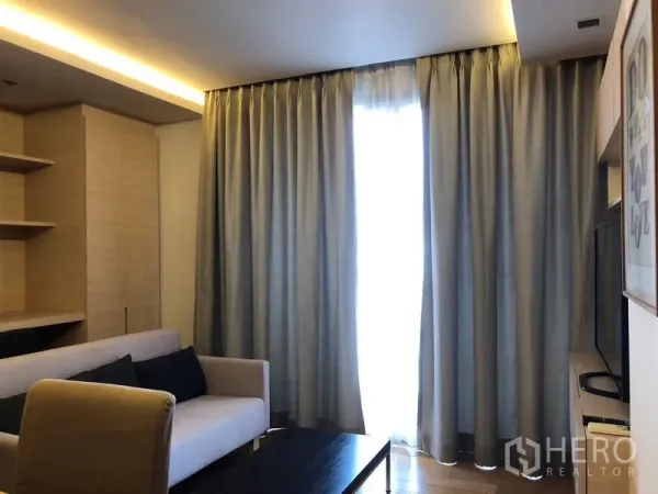 Condominium for rent in Watthana, Bangkok - Cozy living room with a light sofa, full-height curtains, and warm cove lighting.