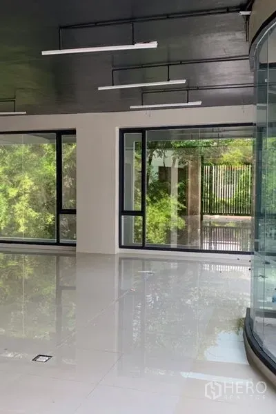 Standalone for rent in Khlong Toei, Bangkok - Bright interior with floor-to-ceiling windows, glossy tiles, and garden views through tinted glass.