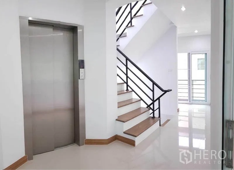 Home Office for rent in Prawet, Bangkok - Close-up of staircase with black handrail beside a stainless steel lift and doors to a small balcony.