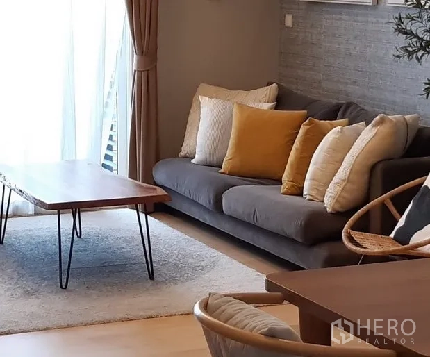 Condominium for rent in Khlong Toei, Bangkok - Bright living room with gray sofa, mustard cushions, wood coffee table and floor-to-ceiling curtains in a modern Bangkok condo near BTS Thonglor.