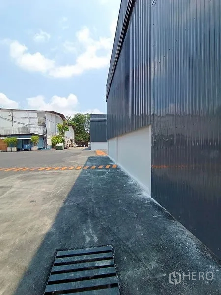 Warehouse for rent in Khlong Toei, Bangkok - Side walkway along gray metal warehouse with drainage grate and traffic hump.