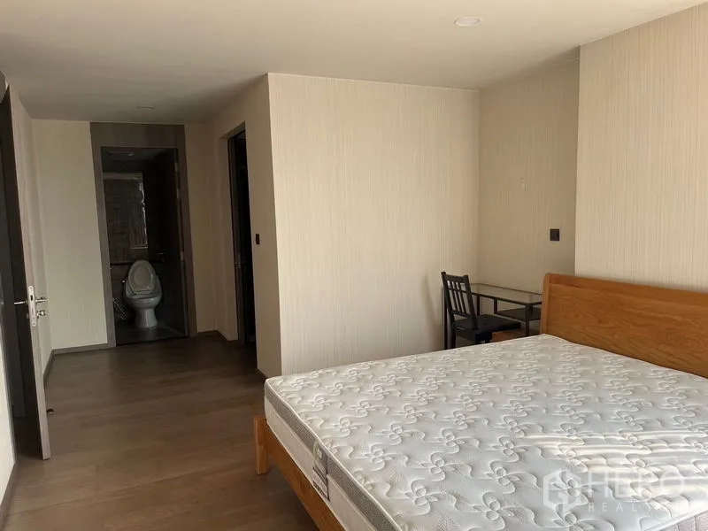 公寓 出租在Pathum Wan, Bangkok - 宽敞卧室，木床与学习角，走廊通向浴室。