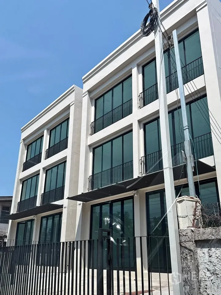 Home Office for rent in Bang Na, Bangkok - Modern three-storey home office exterior with full-height glass windows and balconies behind a metal fence.