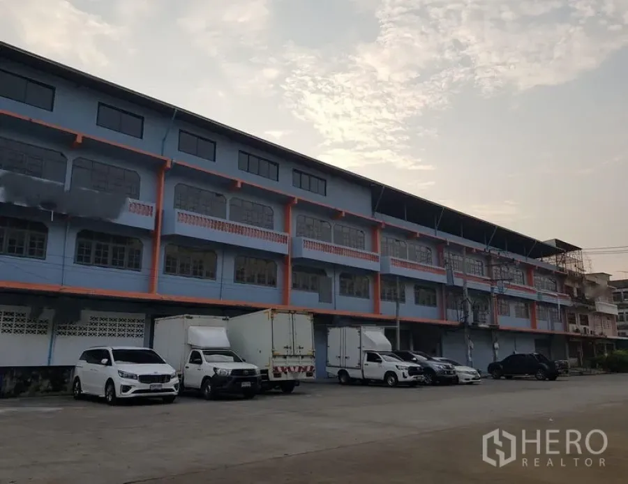 Warehouse for rent in Nong Khaem, Bangkok - Exterior of a multi-storey warehouse with truck and car parking area.