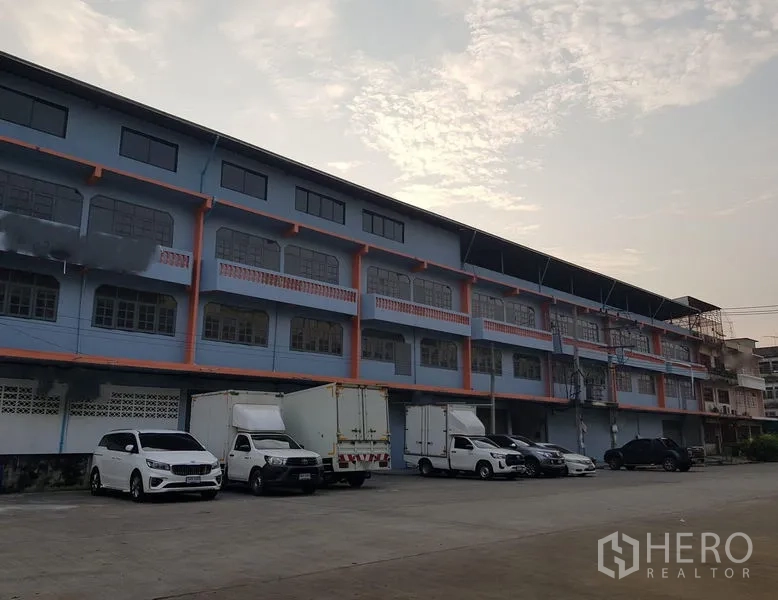 Warehouse for rent in Nong Khaem, Bangkok - Exterior of a multi-storey warehouse with truck and car parking area.