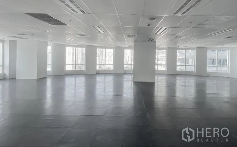 สำนักงาน ให้เช่า - ชั้นมุมสำนักงานสว่าง มีเสาโครงสร้าง เพดานฝ้าทีบาร์ และหน้าต่างบานใหญ่เห็นเส้นขอบฟ้ากรุงเทพฯ
