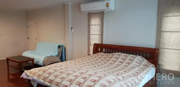 独立式住宅 出租在Phra Khanong, Bangkok - 宽敞卧室，木质床与格纹被套，壁挂空调，沙发与小茶几，窗帘遮光。
