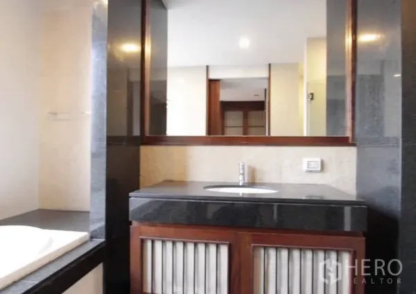 Detached House for rent in Khlong Toei, Bangkok - Contemporary bathroom with a wide mirror, dark stone countertop and wooden vanity cabinetry.