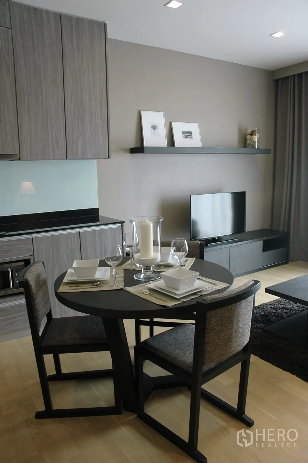 Condominium for rent in Watthana, Bangkok - Open-plan dining area and kitchenette with a round table set, wood cabinetry and a TV console.