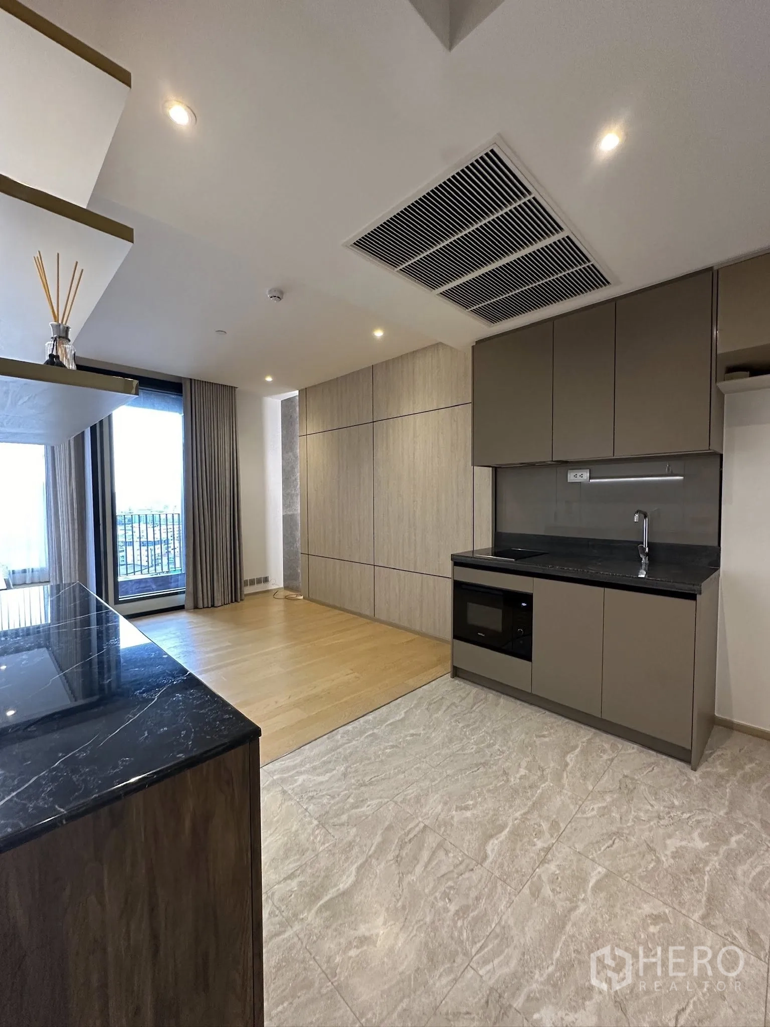 Condominium for sale in Din Daeng, Bangkok - Open-plan kitchen and living area with black stone countertops, wood floors, and balcony window.