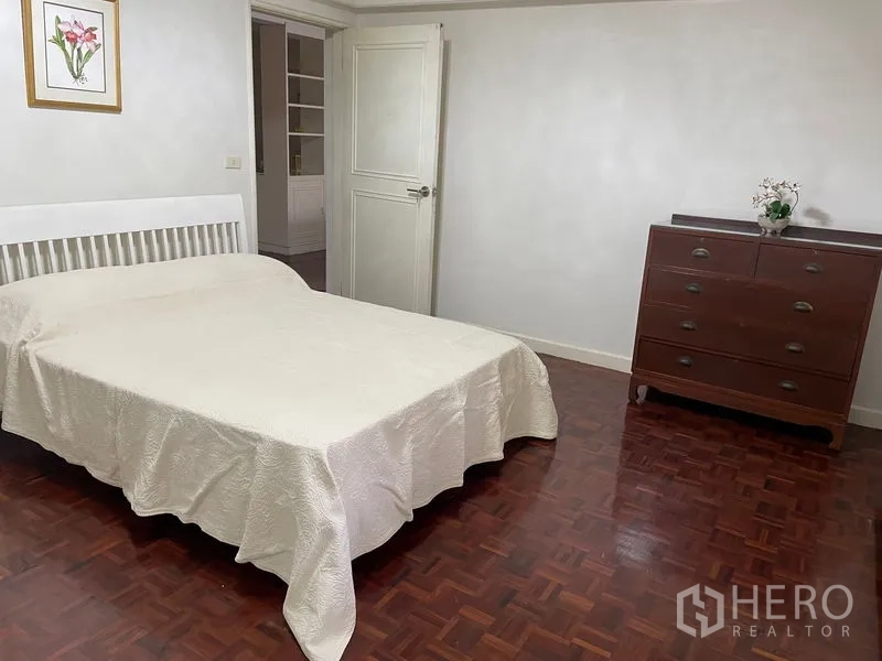 Apartment for rent in Watthana, Bangkok - Spacious bedroom with a double bed and wooden dresser on parquet floors.
