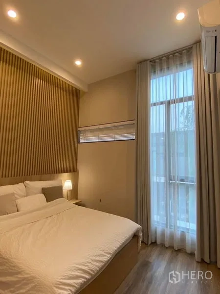 联排别墅 出租在Saphan Sung, Bangkok - 温馨卧室，木质背景墙，落地窗帘与柔和灯光，并配空调。