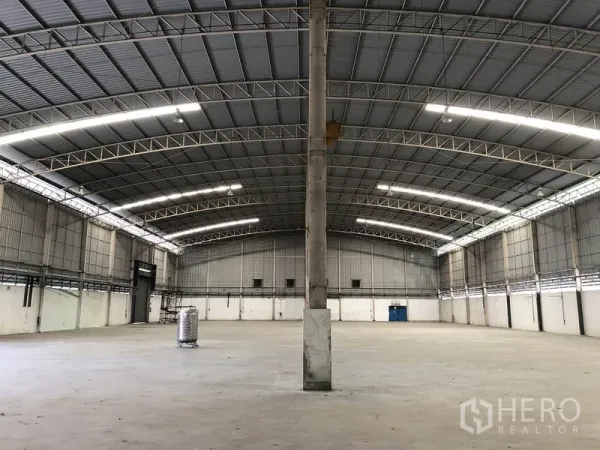 Factory for rent in Phra Nakhon Si Ayutthaya - Open factory floor with central columns beneath a curved metal truss roof and bright strip lighting.
