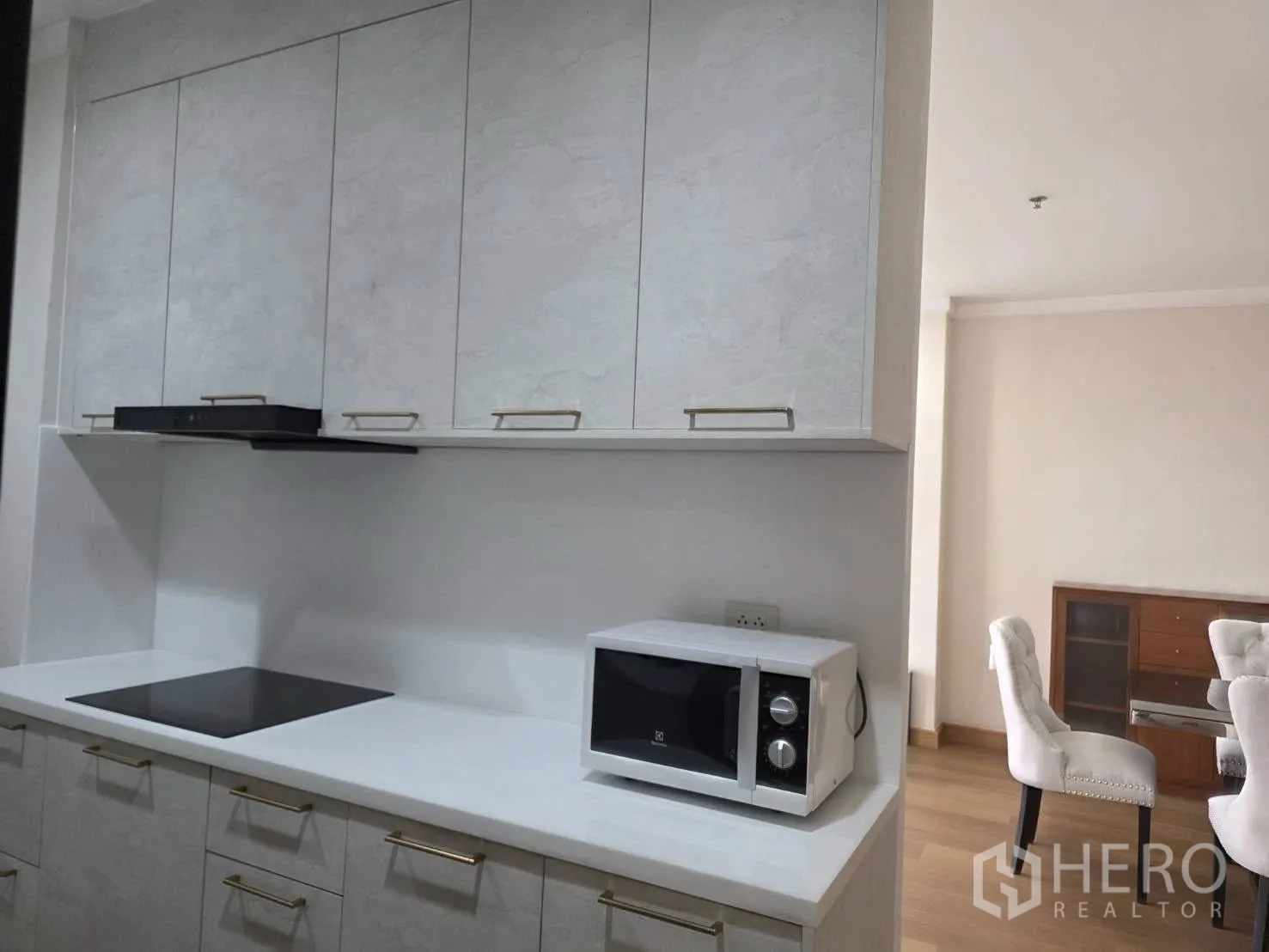 Condominium for rent in Khlong Toei, Bangkok - Kitchen cooktop and upper cabinets with a microwave on the countertop.