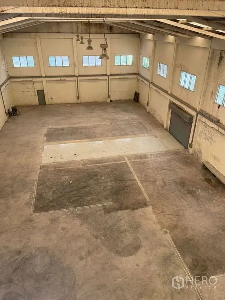 Warehouse for rent in Samut Sakhon - Spacious high-ceiling warehouse with concrete floor, skylights, side windows and a roller shutter door.