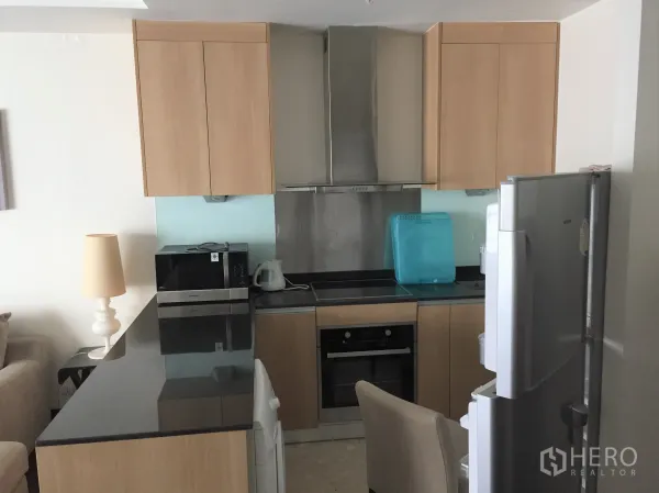 Condominium for rent in Sathon, Bangkok - Modern L-shaped kitchen with black stone countertop, built-in oven, range hood and fridge.