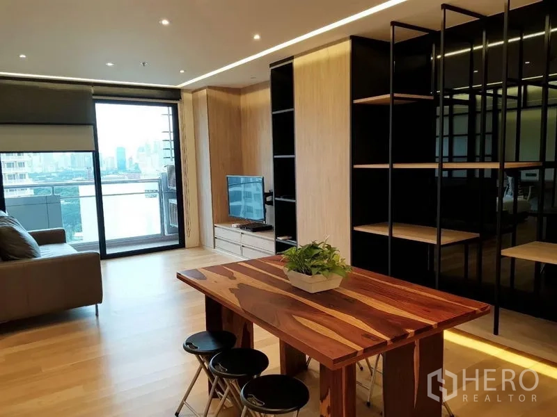 Condominium for rent in Bang Rak, Bangkok - Living area with solid wood dining table, sofa, open shelving and access to the balcony.