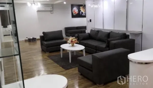 Condominium for rent in Khlong Toei, Bangkok - Spacious living room with grey sofas, white coffee table, hardwood floors and wall art.