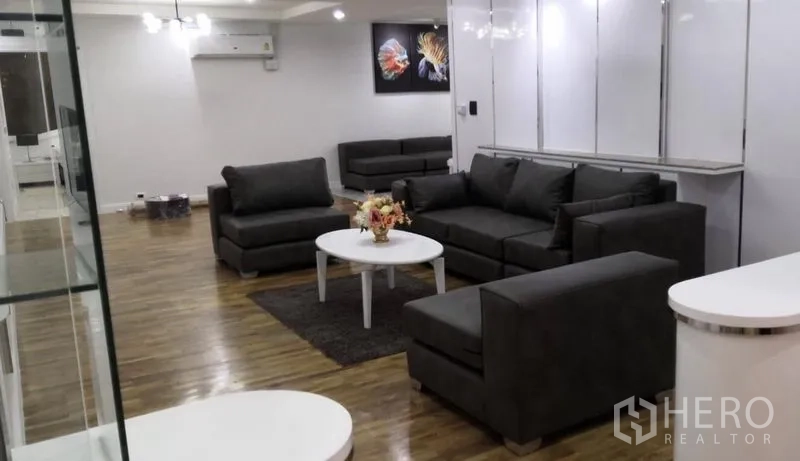 Condominium for rent in Khlong Toei, Bangkok - Spacious living room with grey sofas, white coffee table, hardwood floors and wall art.