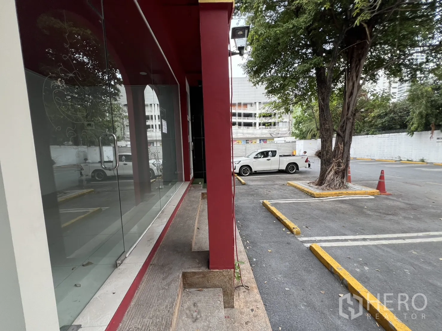 พื้นที่ขายของ for rent in Watthana, Bangkok - ทางเดินข้างกระจกโชว์สินค้าสูงจรดเพดาน เชื่อมสู่ลานจอดรถโล่งมีต้นไม้ใหญ่