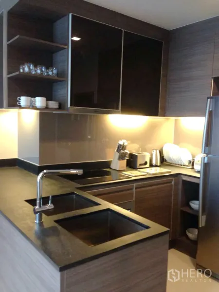 Condominium for rent in Khlong Toei, Bangkok - Modern U-shaped kitchen with stone countertops, induction hob, ample cabinets and stainless fridge.
