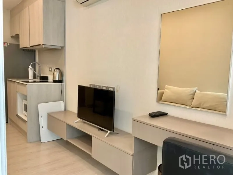 Condominium for sale in Khlong Toei, Bangkok - Living area with TV console, work desk and large wall mirror next to the kitchen.