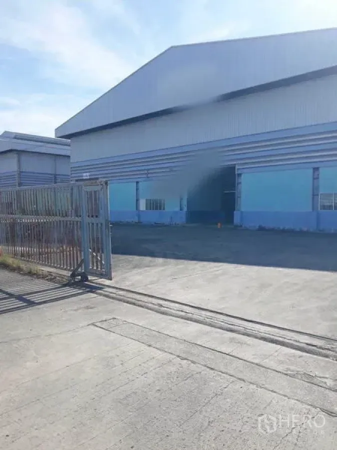 Factory for rent in Samut Prakan - Gated entrance to the industrial warehouse with sliding metal gate and parking apron.