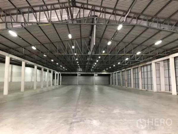 Warehouse for rent in Nonthaburi - Spacious warehouse interior with high steel-truss roof, bright LED lighting, polished concrete floor and multiple roller-shutter loading bays.