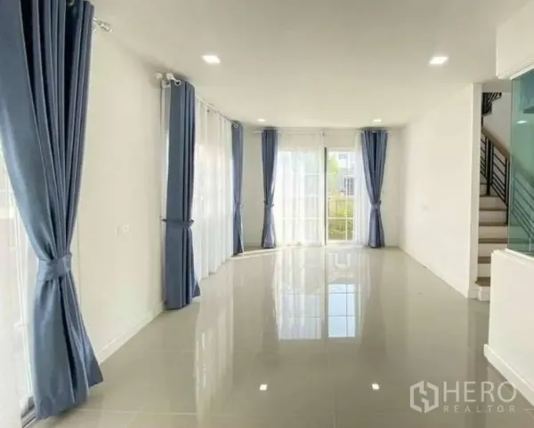 Detached House for sale in Bang Khen, Bangkok - Spacious living and dining area with glossy tile floors, large windows and blue curtains bringing in natural light.