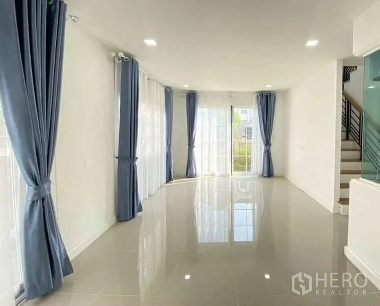 Detached House for sale in Bang Khen, Bangkok - Spacious living and dining area with glossy tile floors, large windows and blue curtains bringing in natural light.