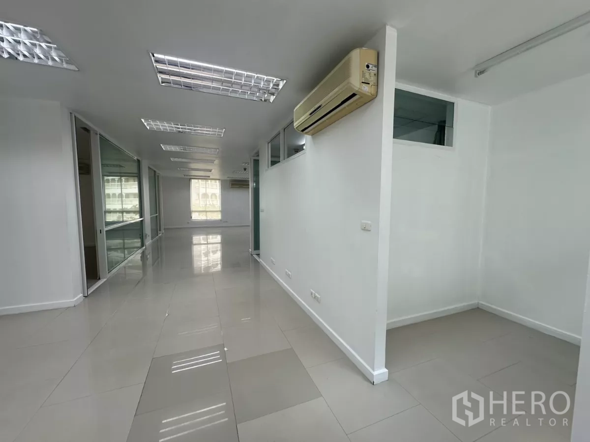 Office Space for rent in Huai Khwang, Bangkok - Bright open-plan office with glass-partitioned rooms, tiled floors, split AC units and fluorescent lighting.