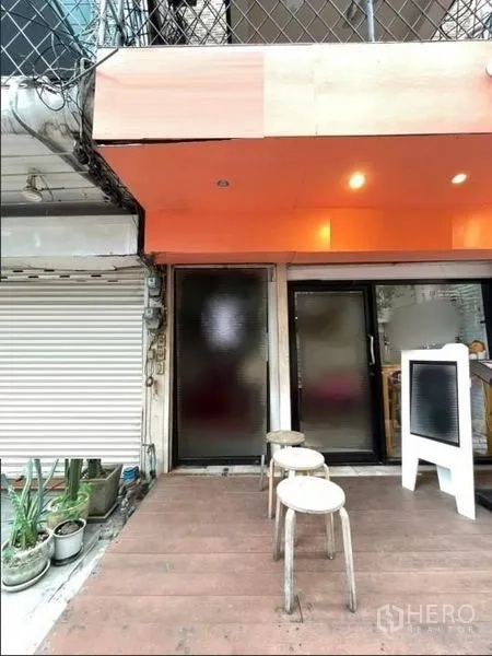 店屋 出租在Phaya Thai, Bangkok - 店屋一层入口，橙色雨棚、毛玻璃门、小木平台与凳子。
