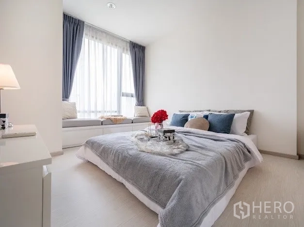 Condominium for sale in Khlong Toei, Bangkok - Spacious bedroom with window seat, soft grey bedding, and natural light.