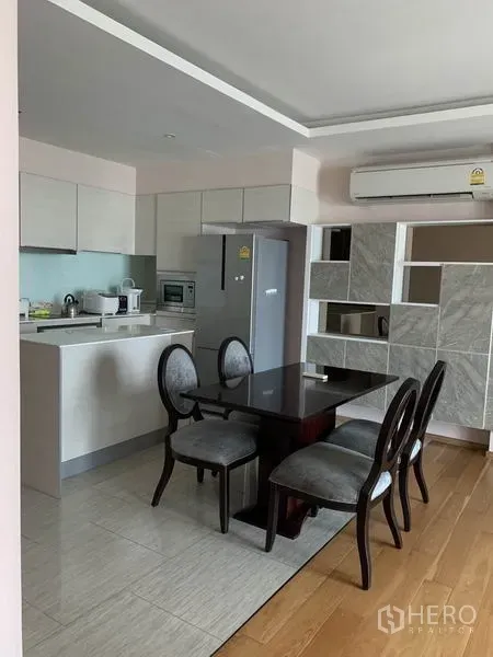 Condominium for rent in Watthana, Bangkok - Open-plan kitchen with white cabinets, four-seat dining table, refrigerator and air conditioner in a Bangkok condo.