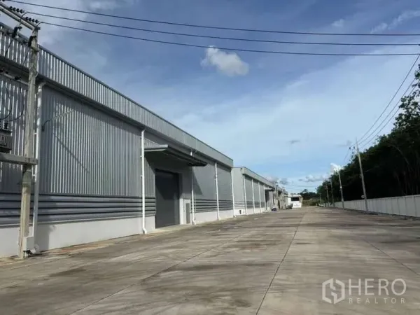 货栈 出租在Nikhom Phatthana, Rayong - 罗勇工业区内的现代仓库外观，带卷闸门与宽阔混凝土车道