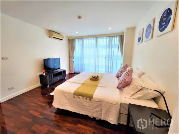 Condominium for rent in Bang Rak, Bangkok - Cozy bedroom with king bed, TV console, air-conditioning and full-height windows.