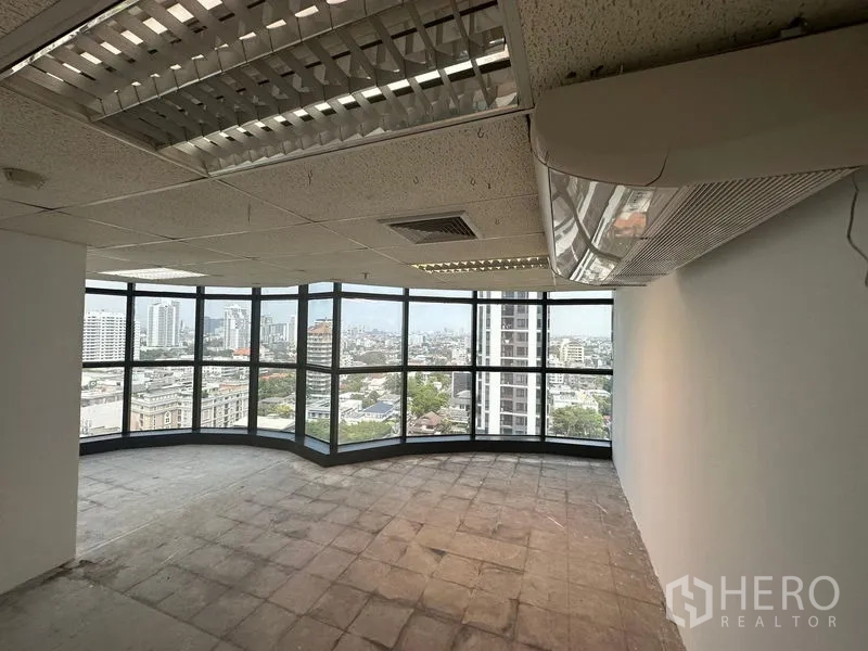 办公空间 出租 - 转角办公室，环幕落地窗、吊顶灯具与壁挂空调，俯瞰曼谷天际线。