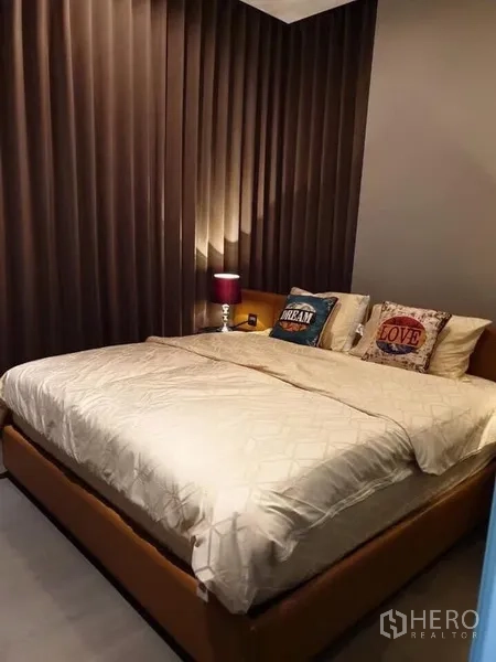 คอนโด ให้เช่าในHuai Khwang, Bangkok - ห้องนอนเตียงคิงไซซ์ โคมไฟหัวเตียง และผ้าม่านทึบสูงจรดเพดาน