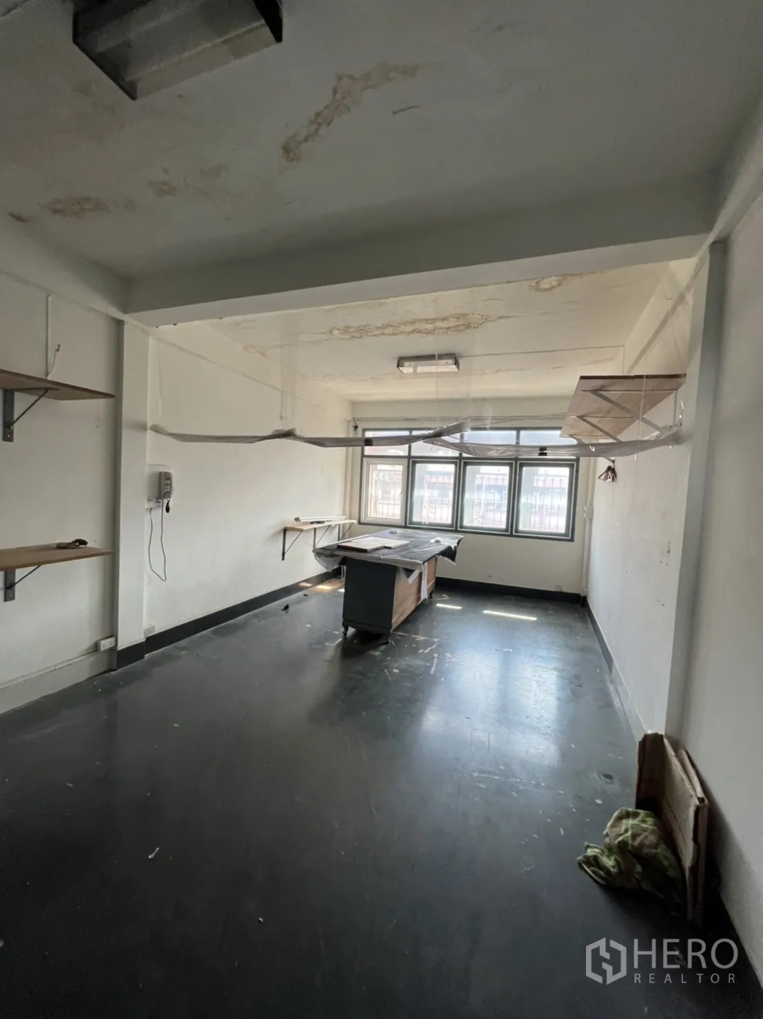Shophouse for rent or sale in Watthana, Bangkok - Workroom with worn ceiling, wall shelves and a central table.