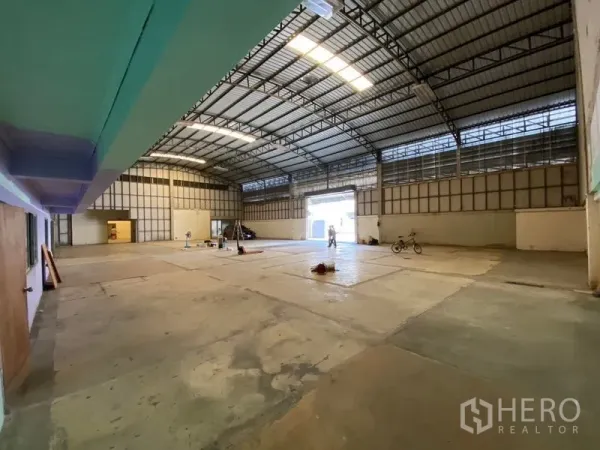 Warehouse for rent in Bueng Kum, Bangkok - Open-plan warehouse with high truss roof, natural light panels and a large roller shutter door for loading.