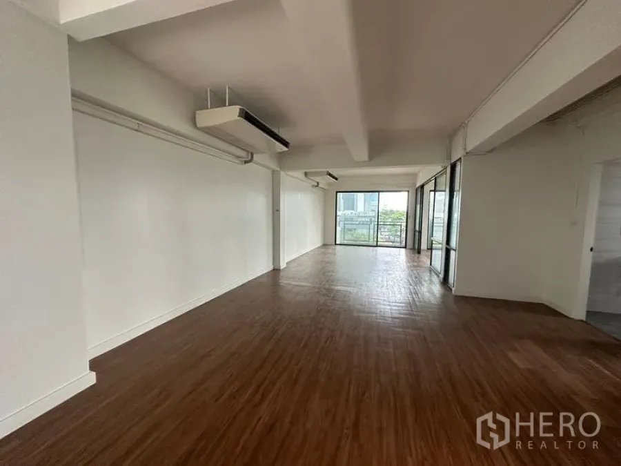 Office Space for rent in Sathon, Bangkok - Long open-plan area with ceiling air conditioners, white walls, and sliding doors opening to an outdoor balcony.