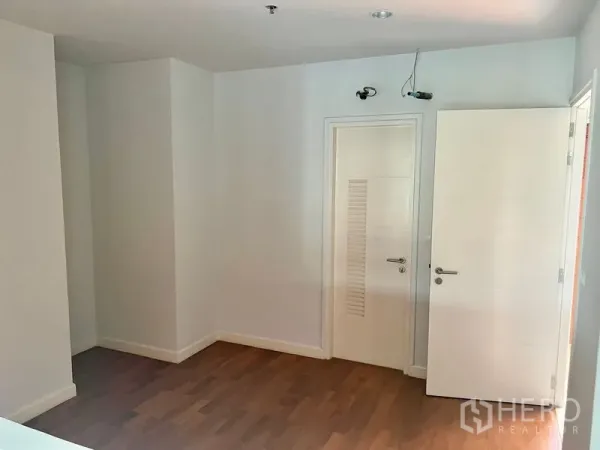 Condominium for rent in Bang Kho Laem, Bangkok - Empty bedroom with warm wood flooring, white walls, and modern white doors.