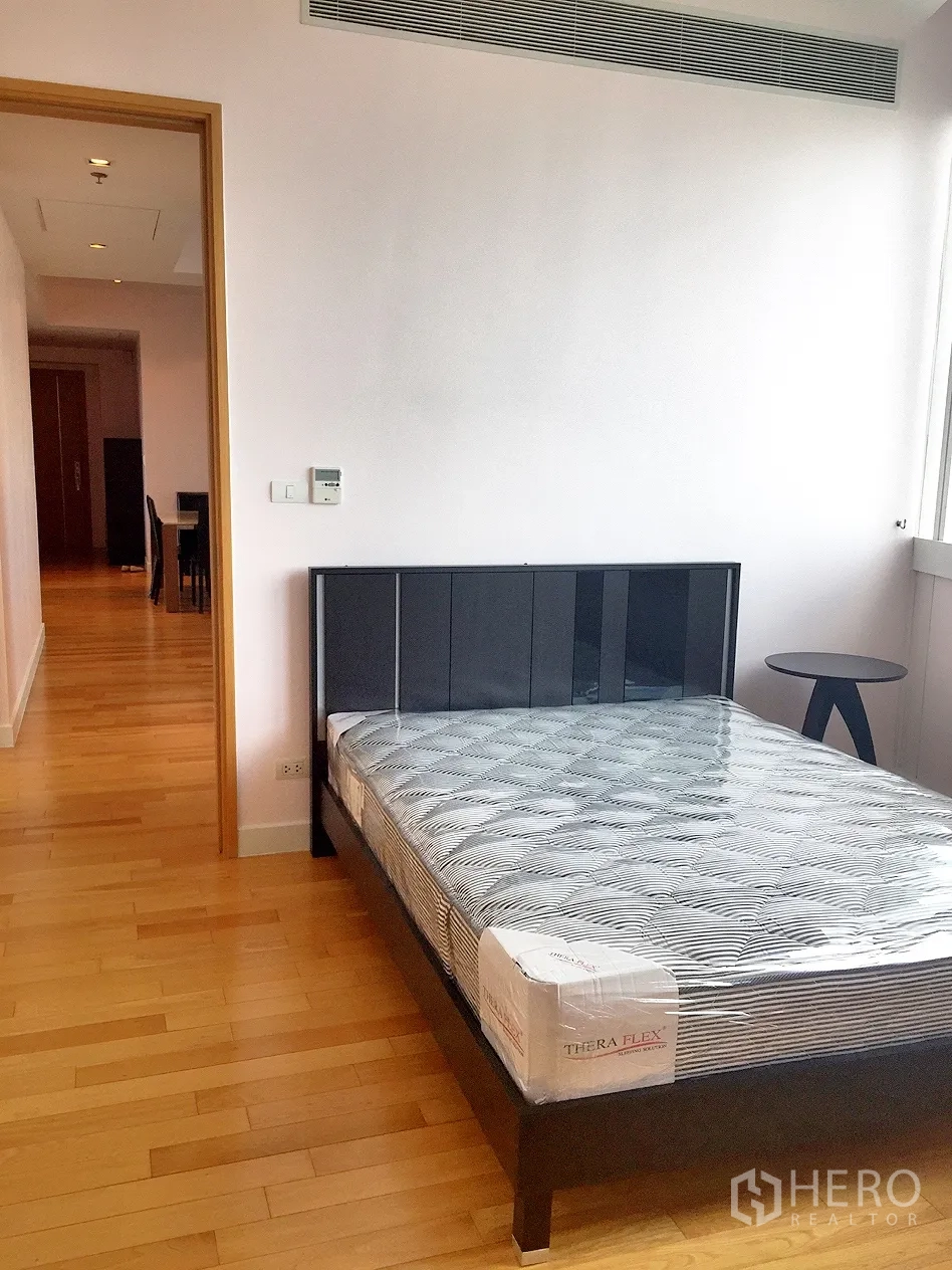 Condominium for rent in Khlong Toei, Bangkok - Bright bedroom with wood flooring, a modern bed frame and a large window.
